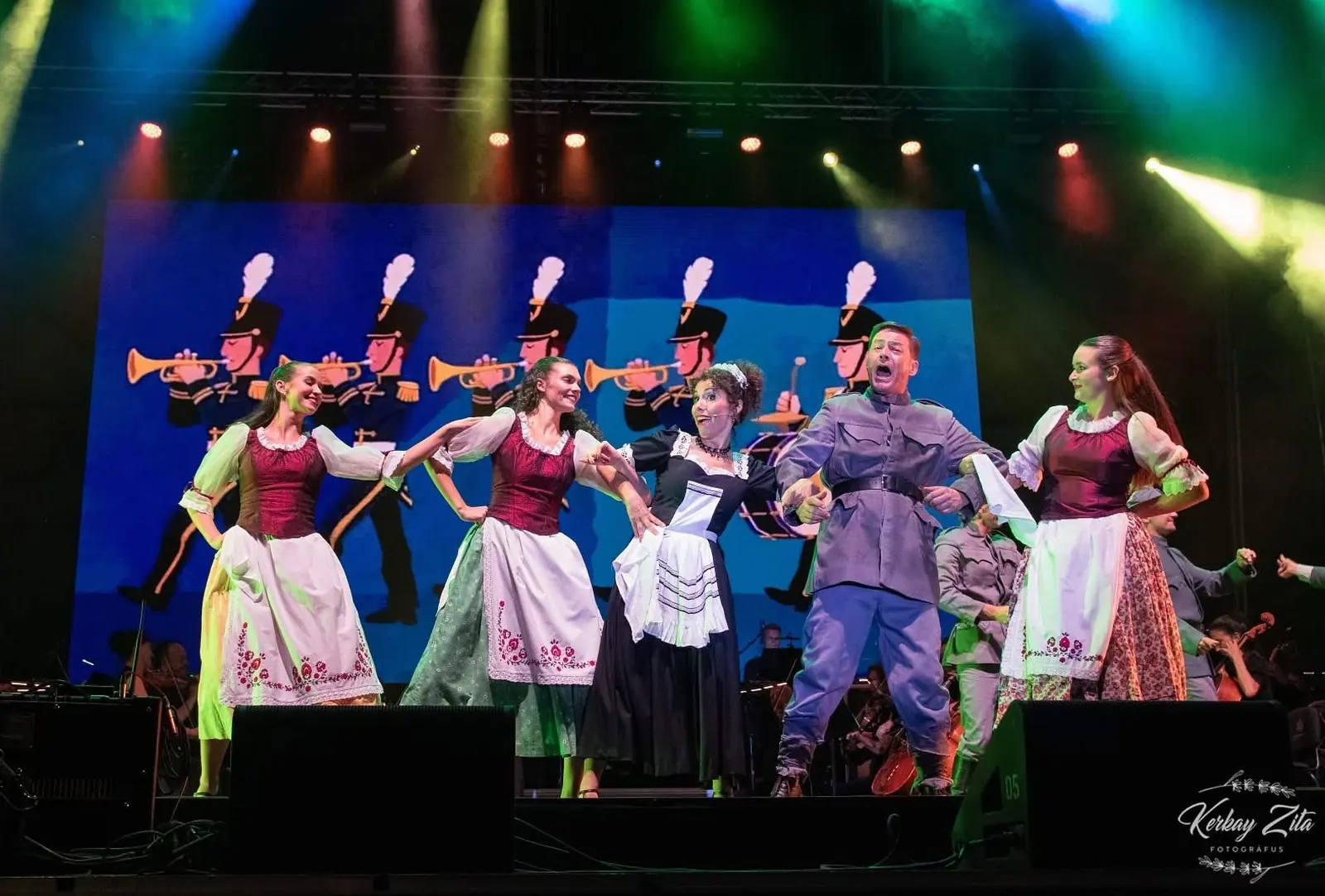 Folk dancers on stage with the projected military band on the LED wall behind them